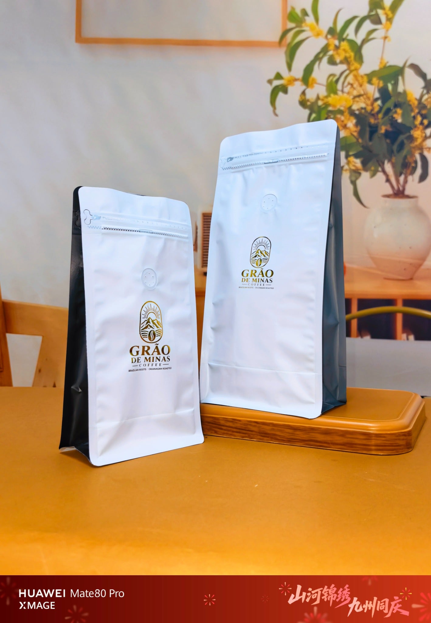 Two white-front coffee pouches with black side gussets, gold GRAO DE MINAS logos, resealable zippers and visible degassing valves